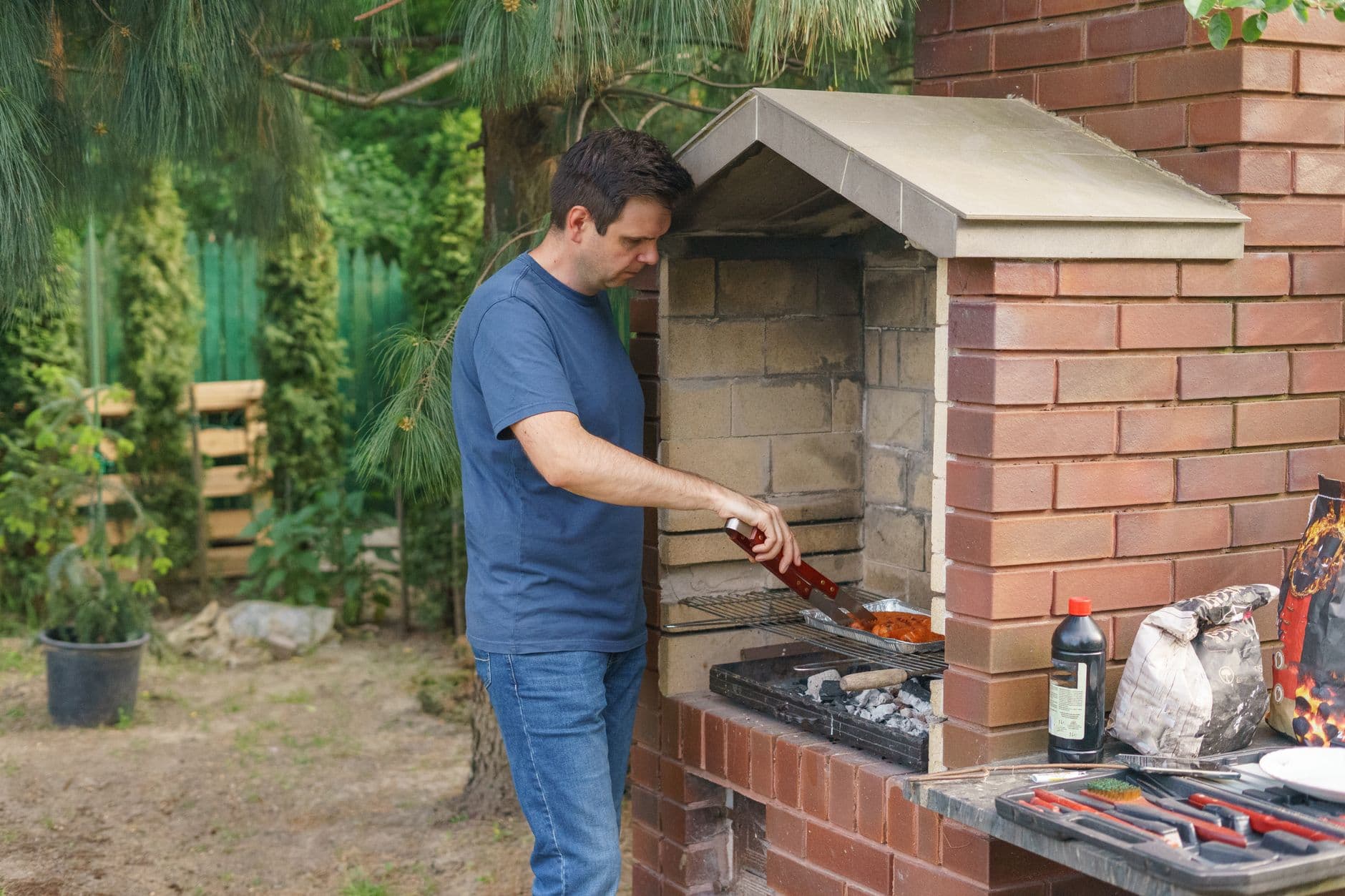 A man grills meat on a brick barbecue in the garden, showcasing outdoor cooking and leisure activity.