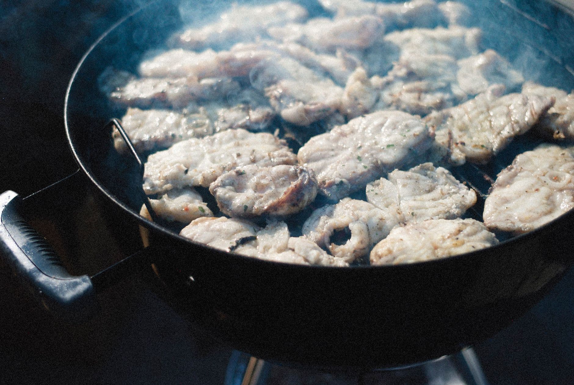 Close-up of fish fillets sizzling on a barbecue grill outdoors, exuding a smoky aroma.